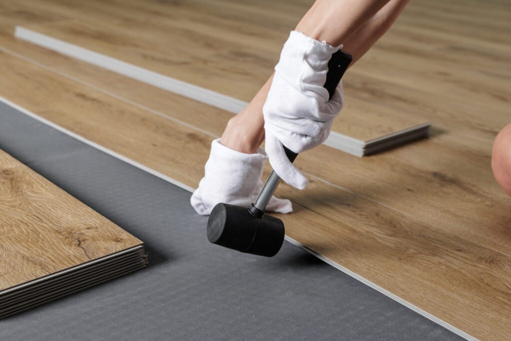 close up aligning spc vinyl plank on underlayment with rubber mallet